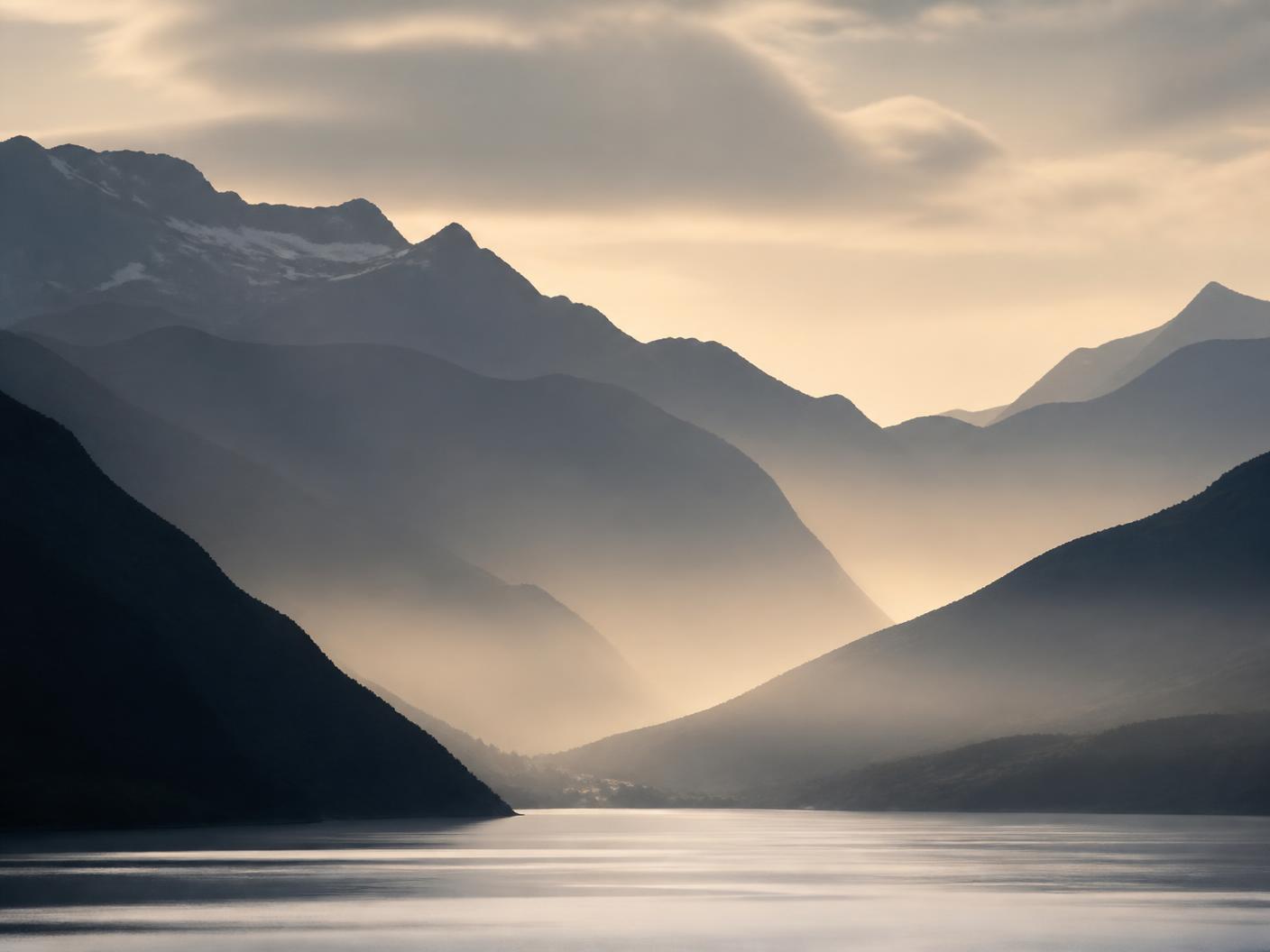 Valle de montaña al amanecer con cordilleras superpuestas y agua en calma